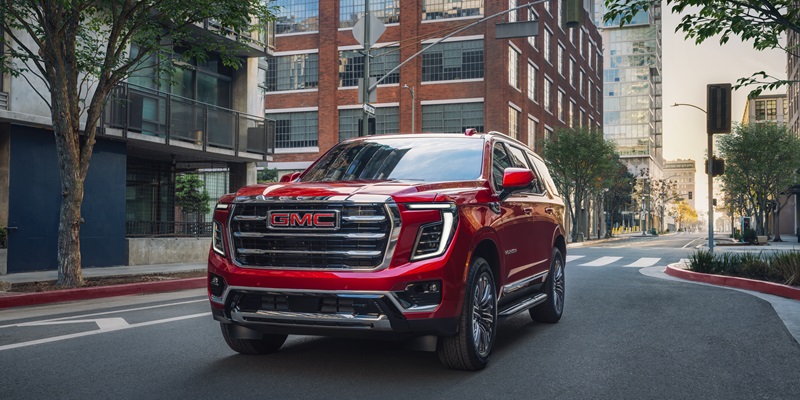 A 2020 GMC Yukon Denali driving down a city street in Bryant, AR, showcasing its sleek design and urban setting.