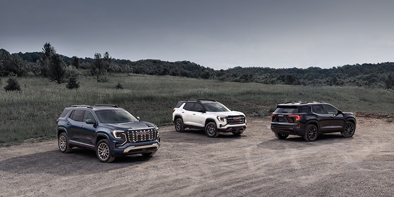 Three GMC SUVs parked on a dirt road, surrounded by greenery and open space.