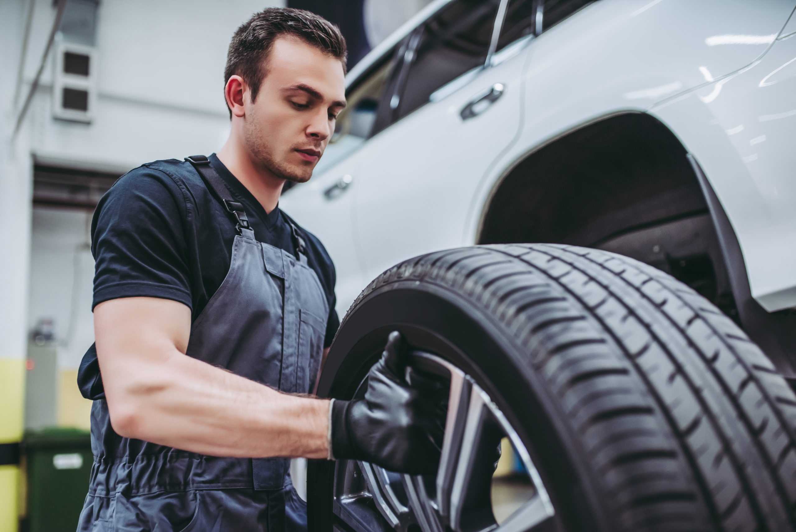A mechanic in a gray apron replaces a tire on a vehicle in a garage.
