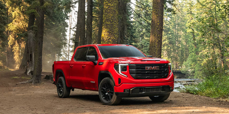 A GMC Sierra 1500 parked amidst trees in a wooded area, showcasing its rugged design and outdoor capability.