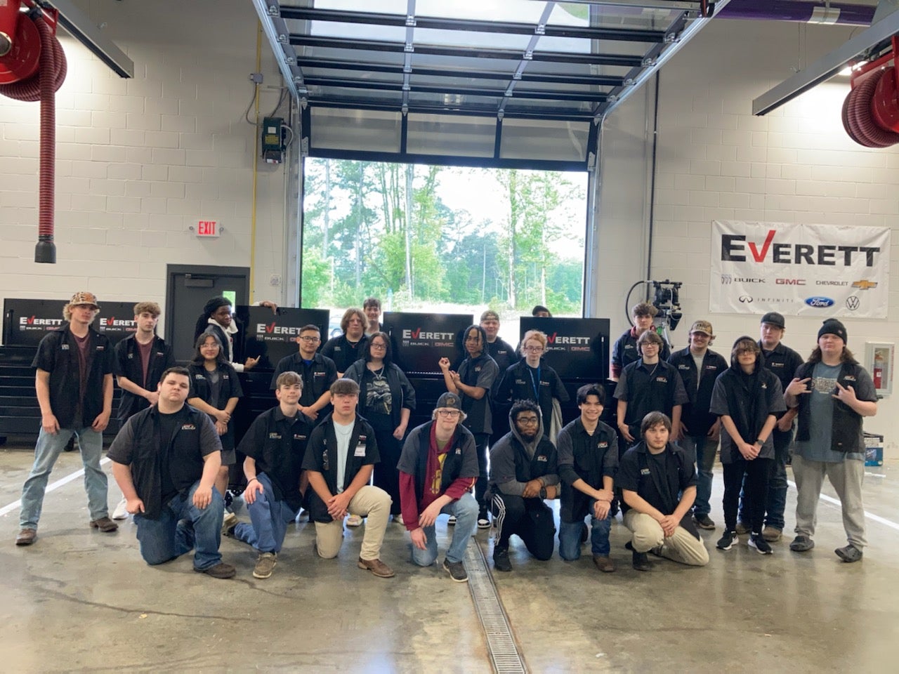 A group of young athletes in baseball uniforms posing for a photo on a field at night, holding a sign that reads Everett.