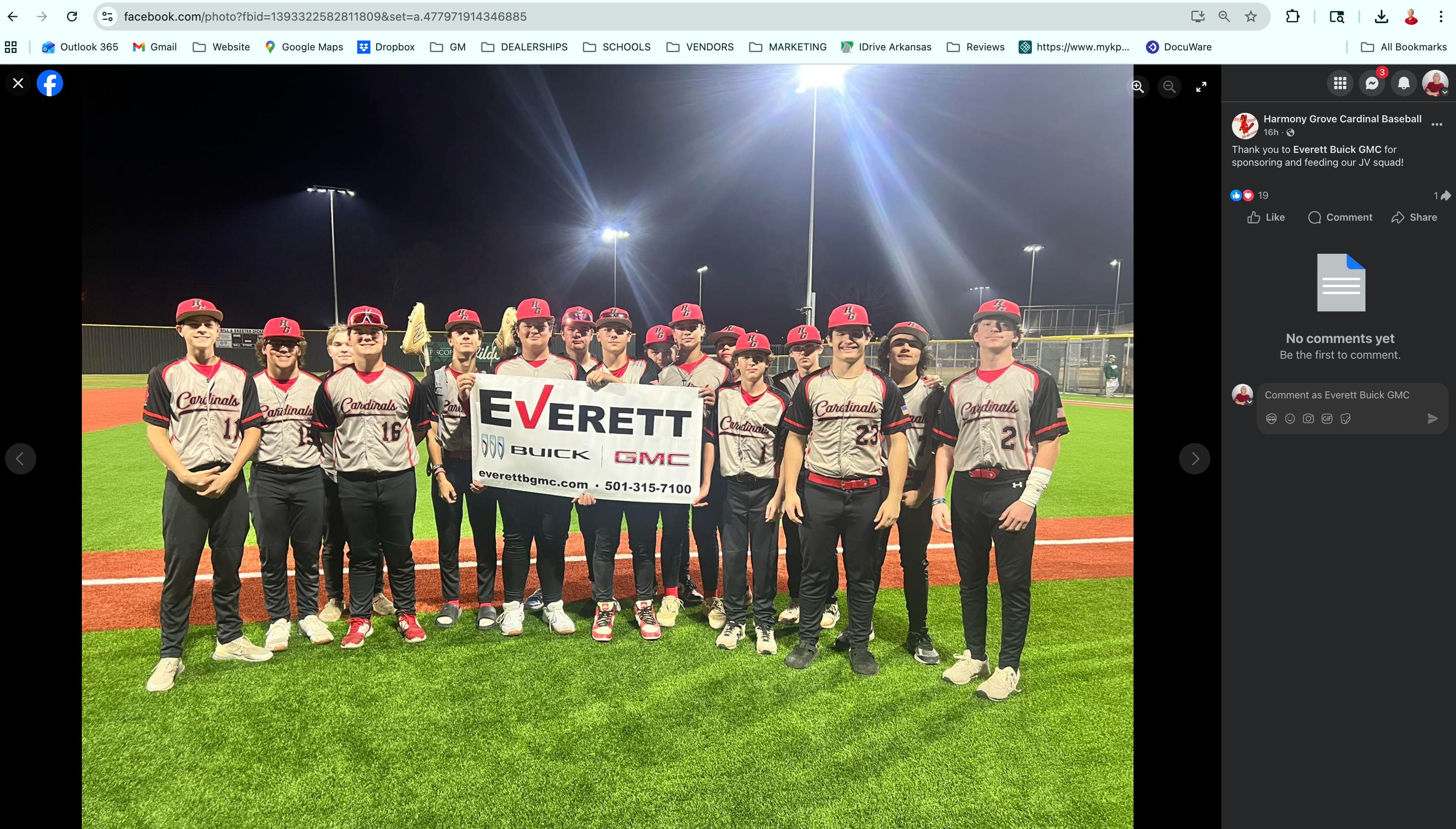 A group of young athletes in baseball uniforms posing for a photo on a field at night, holding a sign that reads Everett.
