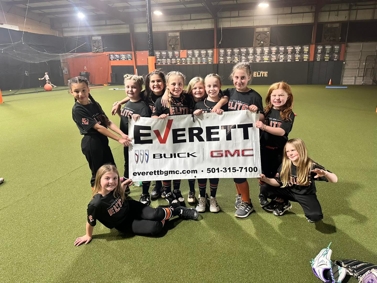 A group of young athletes in black sports uniforms posing together, holding a sign for Everett Buick GMC.