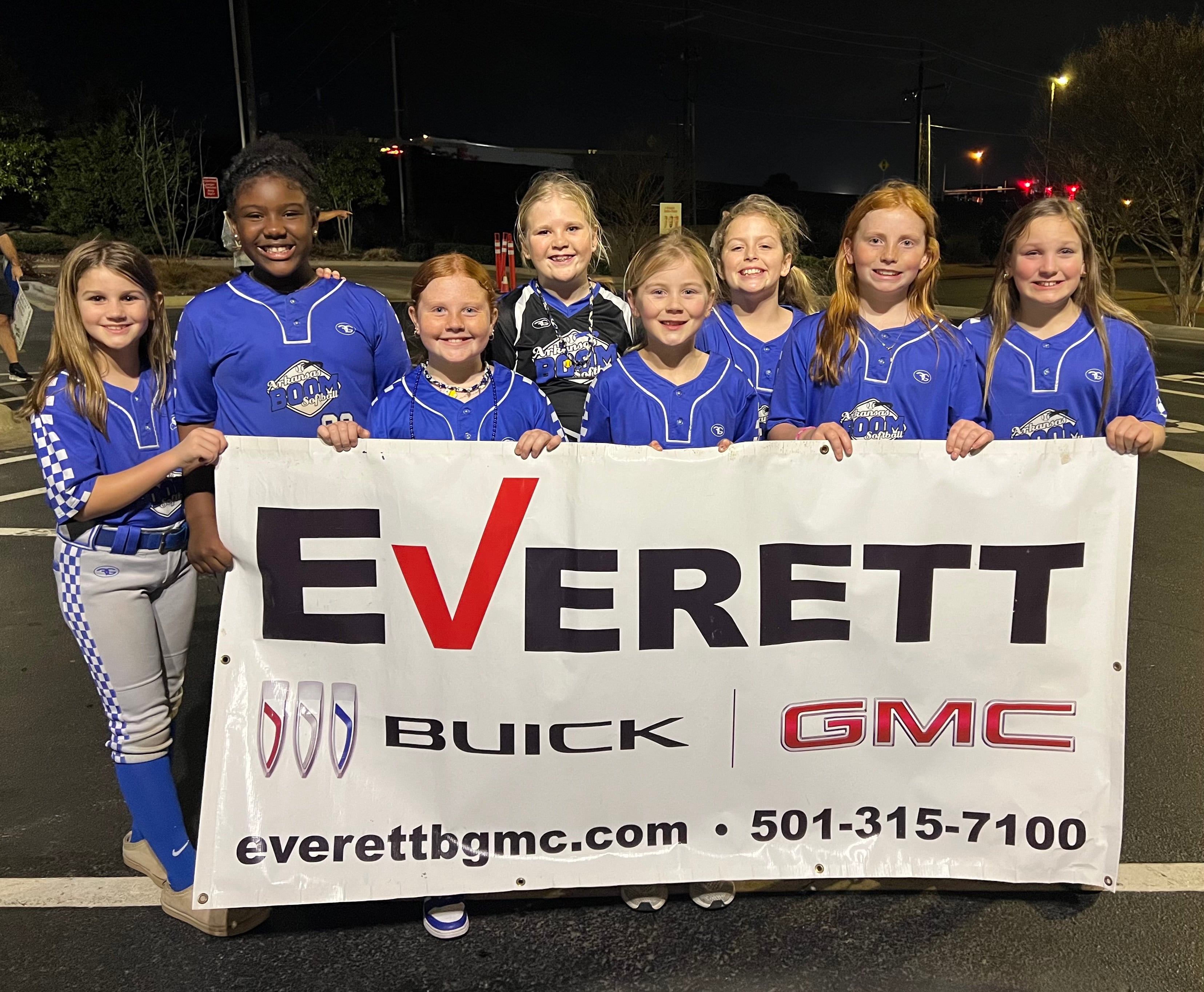 A group of eight young girls in matching blue and gray sports uniforms pose together while holding a large banner for Everett Buick GMC.