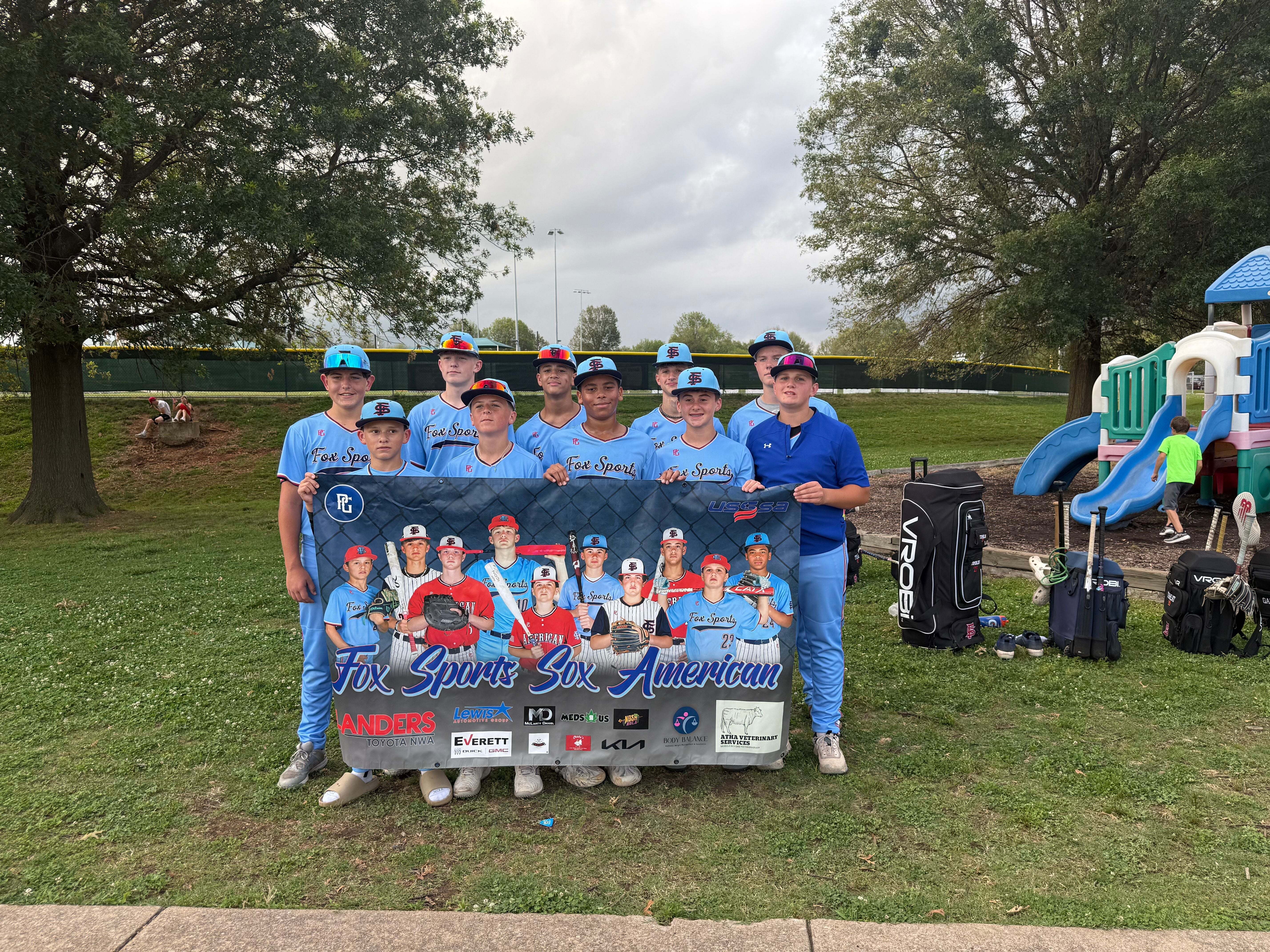 Youth baseball team standing together outdoors holding a team banner.